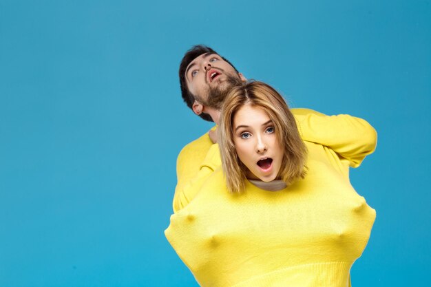 Pareja joven hermosa en un suéter amarillo posando sonriendo divirtiéndose en azul