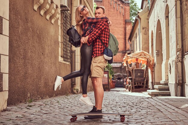 Pareja joven hipster, patinador guapo y su novia abrazados mientras están de pie en las viejas calles estrechas de Europa.