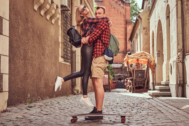 Pareja joven hipster, patinador guapo y su novia abrazados mientras están de pie en las viejas calles estrechas de Europa.