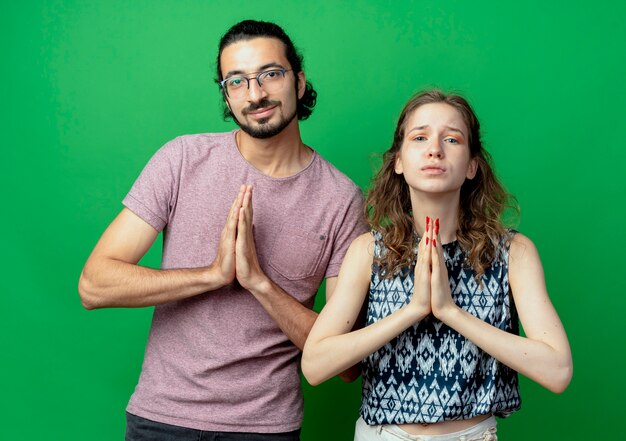 pareja joven, hombre y mujer, manos de valor en cartera, juntos, en, namaste, gesto, como, rezar, posición, encima, pared verde