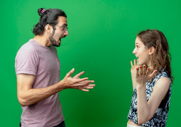 Foto gratuita pareja joven hombre y mujer mirándose feliz y emocionado de pie sobre la pared verde