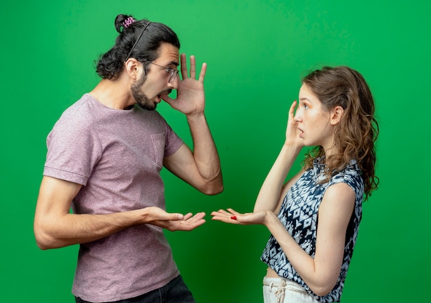 Foto gratuita pareja joven, hombre y mujer, mirarse, estar confundido, posición, encima, pared verde