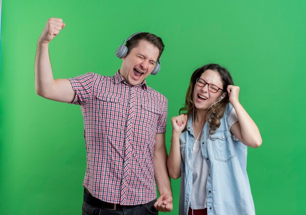 Pareja joven hombre y mujer en ropa casual con auriculares felices y emocionados disfrutando de su música favorita en verde