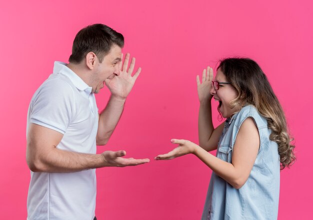 Pareja joven hombre y mujer en ropa casual peleando gritando el uno al otro sobre rosa