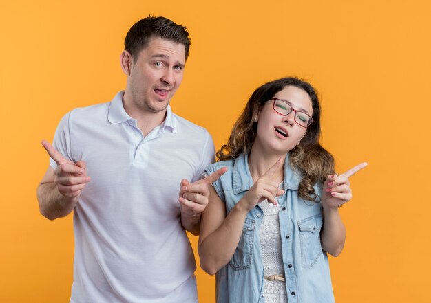 Pareja joven hombre y mujer en ropa casual sonriendo alegremente mostrando los dedos índices alegre y alegre sobre naranja