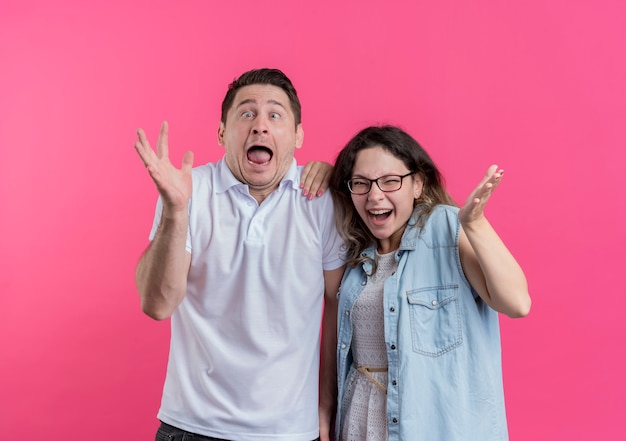 Pareja joven hombre y mujer en ropa casual sorprendido y asombrado loco feliz parado sobre pared rosa