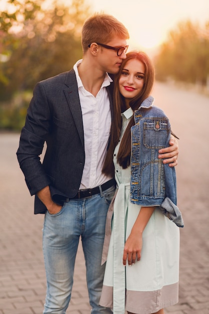 Pareja joven inconformista en el amor al aire libre. Impresionante sensual retrato de joven pareja de moda elegante posando en el atardecer de verano. Bastante joven en chaqueta de jeans y su guapo novio caminando.