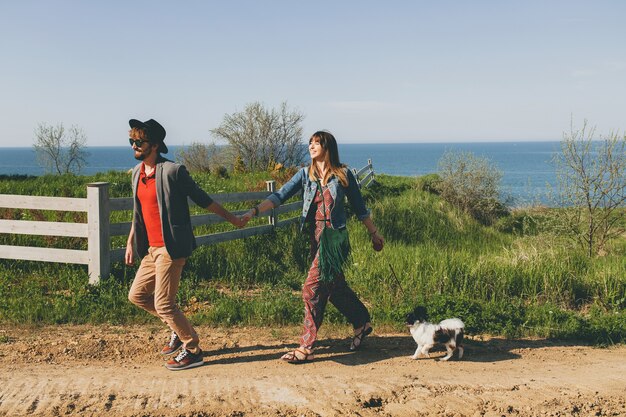 Pareja joven inconformista elegante enamorado caminando con perro en campo, corriendo, divirtiéndose