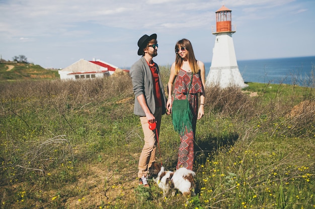 Pareja joven inconformista elegante enamorado caminando con perro en campo