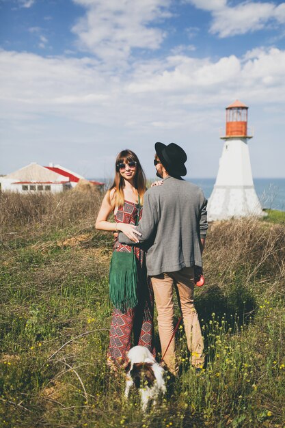 Pareja joven inconformista elegante enamorado caminando con perro en campo