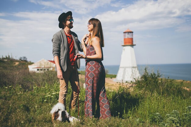 Pareja joven inconformista elegante enamorado caminando con perro en campo