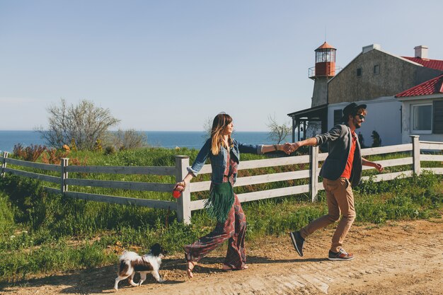 Pareja joven inconformista elegante enamorado caminando con perro en campo