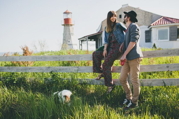 Pareja joven inconformista elegante enamorado caminando con perro en campo