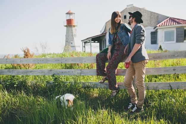 Pareja joven inconformista elegante enamorado caminando con perro en campo