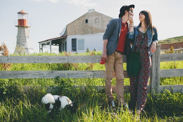 Pareja joven inconformista elegante enamorado caminando con perro en campo