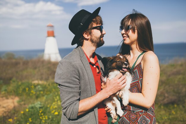 Pareja joven inconformista elegante enamorado caminando con perro en campo