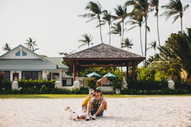 Pareja joven inconformista con estilo enamorado caminando jugando perro cachorro jack russell, playa tropical, traje fresco, estado de ánimo romántico, divirtiéndose, soleado, hombre mujer juntos, horizontal, vacaciones, casa casa villa