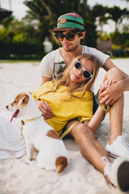 Pareja joven inconformista con estilo enamorado caminando jugando perro cachorro jack russell, playa tropical, traje fresco, estado de ánimo romántico, divirtiéndose, soleado, hombre mujer juntos, horizontal, vacaciones, casa casa villa