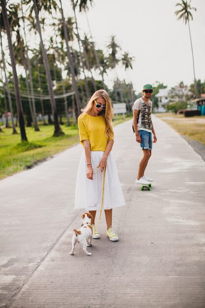 Pareja joven inconformista con estilo enamorado de vacaciones con perro y patineta, divirtiéndose