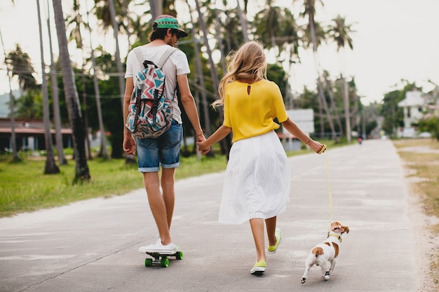 Pareja joven inconformista con estilo enamorado de vacaciones con perro y patineta, divirtiéndose