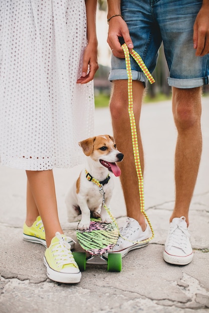 Pareja joven inconformista con estilo enamorado de vacaciones con perro y patineta, divirtiéndose