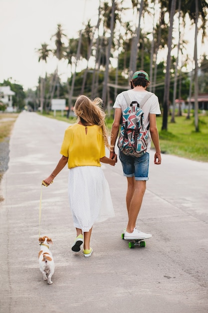 Pareja joven inconformista con estilo enamorado de vacaciones con perro y patineta, divirtiéndose