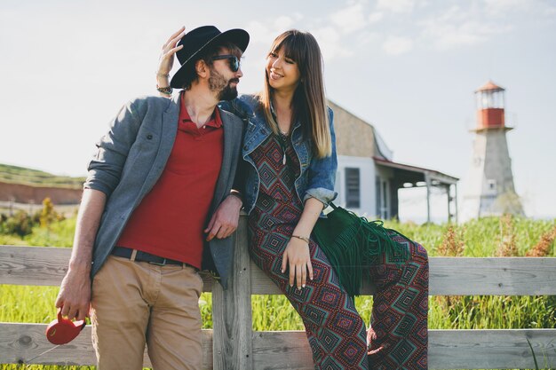 Pareja joven inconformista estilo indie enamorado caminando en el campo, faro en el fondo, vacaciones de verano