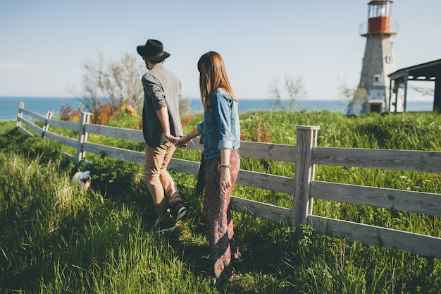 Pareja joven inconformista estilo indie enamorado caminando en el campo, tomados de la mano