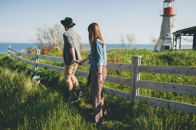 Pareja joven inconformista estilo indie enamorado caminando en el campo, tomados de la mano