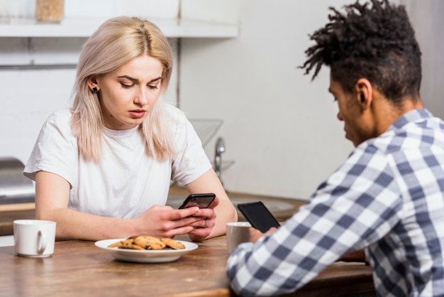 Foto gratuita pareja joven interracial en la mesa de desayuno utilizando teléfono móvil