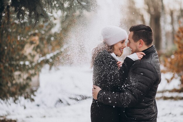 Pareja joven en invierno bajo la nieve que cae del árbol