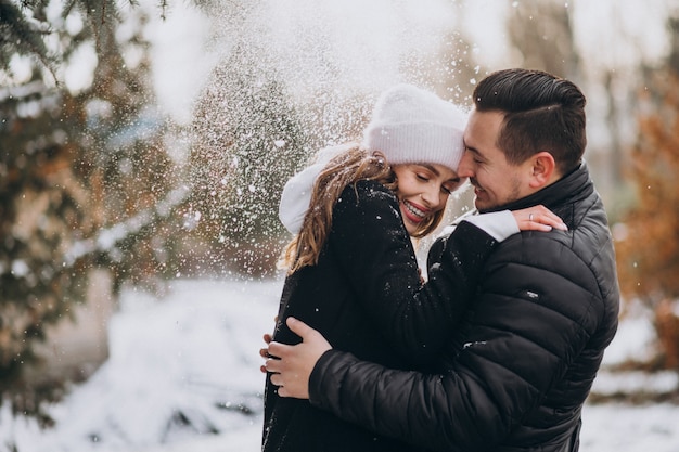 Pareja joven en invierno bajo la nieve que cae del árbol