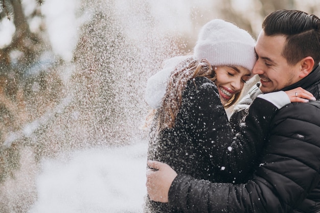 Pareja joven en invierno bajo la nieve que cae del árbol