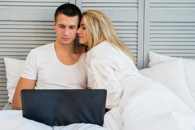Foto gratuito pareja joven con laptop y manta en cama