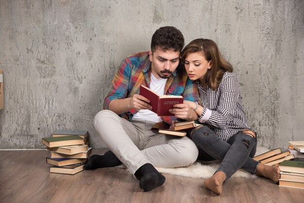 Pareja joven leyendo un libro interesante mientras está sentado en el piso