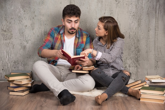 Pareja joven leyendo un libro interesante mientras está sentado en el piso