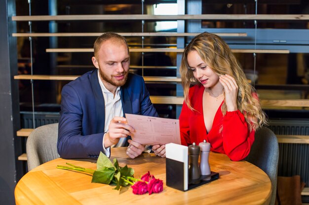 Pareja joven leyendo el menú en la mesa en el restaurante