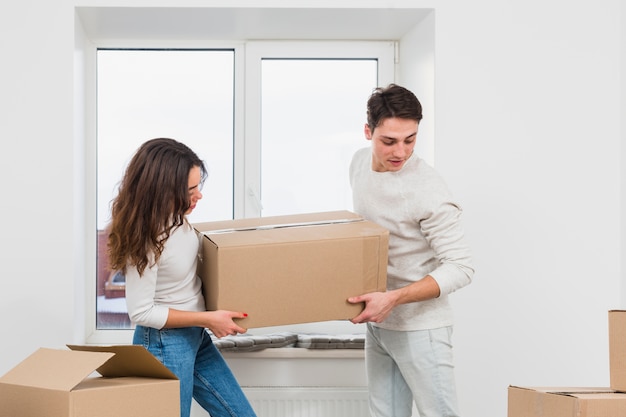 Pareja joven llevando una gran caja de cartón en casa nueva