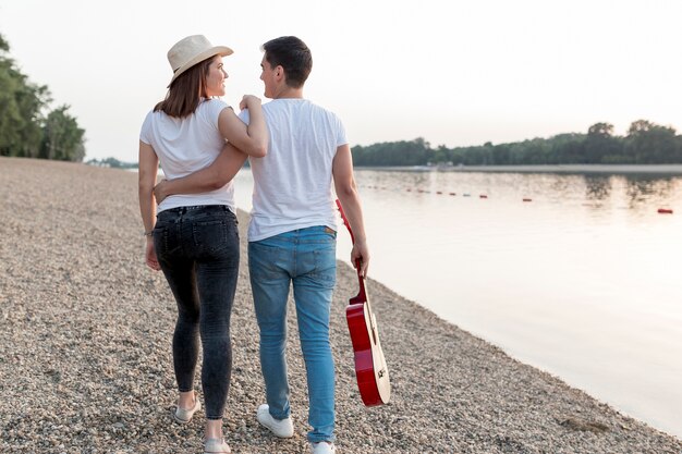 Pareja joven llevando guitarra alejándose en la playa