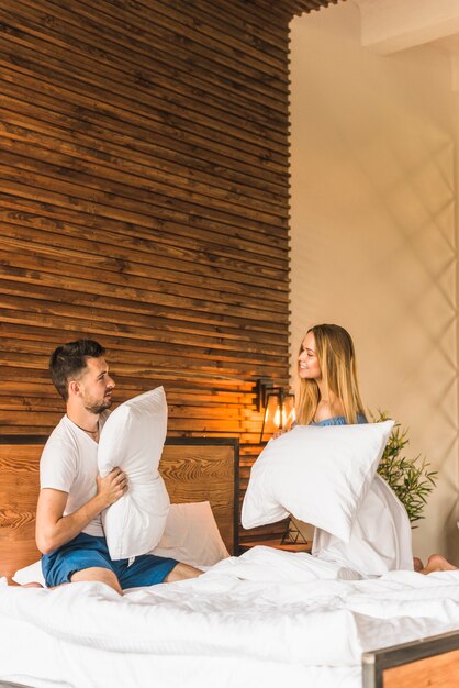 Pareja joven luchando con almohada en la cama