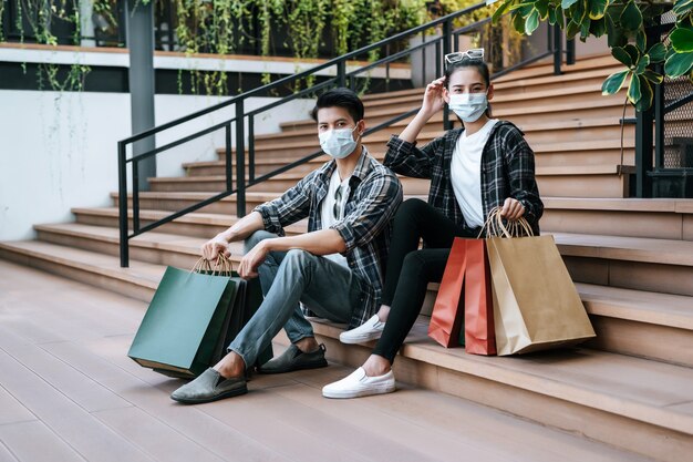 Pareja joven en máscara de protección sosteniendo múltiples bolsas de papel