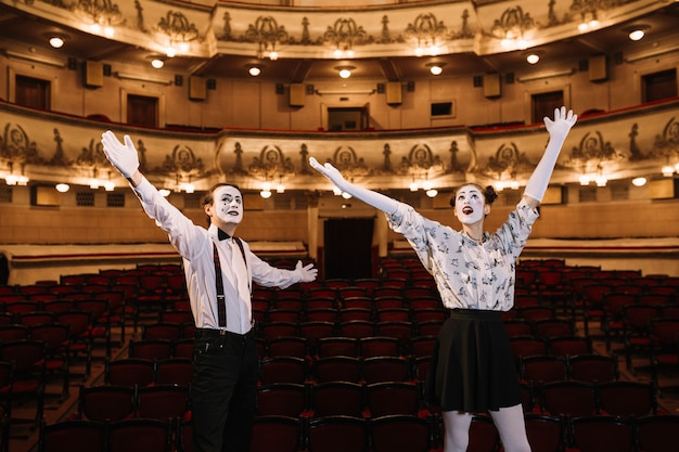 Foto gratuita pareja joven mime de pie en el auditorio levantando los brazos