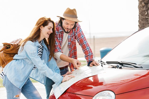 Pareja joven mirando la hoja de ruta en coche rojo