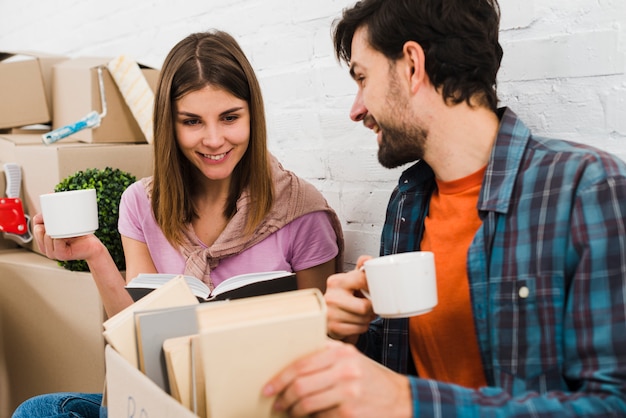 Pareja joven mirando libros en la caja de cartón con tazas de café en la mano