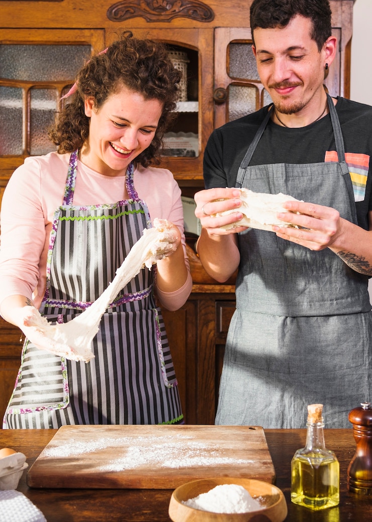 Foto gratuito pareja joven mirando masa amasada en la cocina