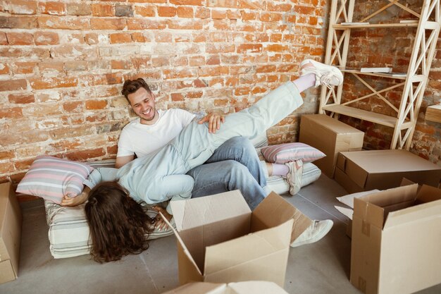 Pareja joven se mudó a una nueva casa o apartamento. Desempacando cajas de cartón juntas, divirtiéndose en el día de la mudanza. Luce feliz, soñadora y confiada. Familia, mudanza, relaciones, primer concepto de hogar.