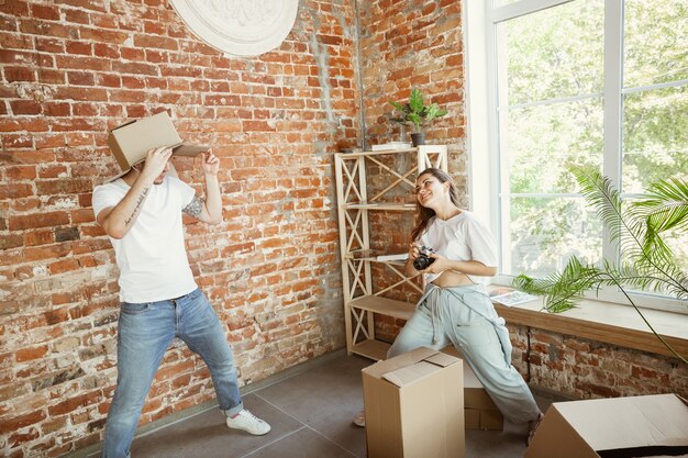 Pareja joven se mudó a una nueva casa o apartamento. Divertirse con cajas de cartón, relajarse después de limpiar y desempacar el día de la mudanza. Verse feliz. Familia, mudanza, relaciones, primer concepto de hogar.