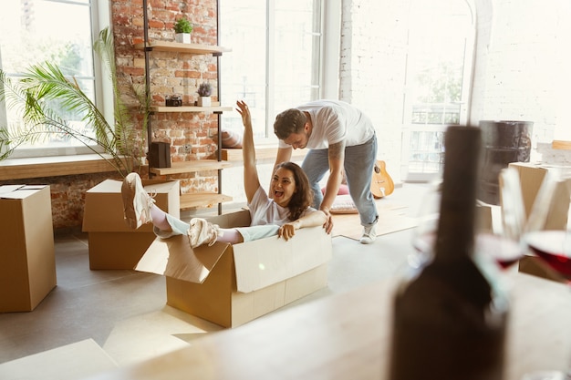 Pareja joven se mudó a una nueva casa o apartamento. Divertirse con cajas de cartón, relajarse después de limpiar y desempacar en el día de la mudanza