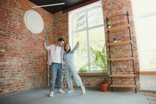 Pareja joven se mudó a una nueva casa o apartamento. Luce feliz y confiado. Familia, mudanza, relaciones, primer concepto de hogar. Pensar en futuras reparaciones y relajarse después de limpiar y desembalar.