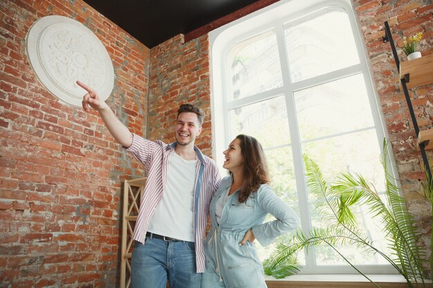 Pareja joven se mudó a una nueva casa o apartamento. Luce feliz y confiado. Familia, mudanza, relaciones, primer concepto de hogar. Pensar en futuras reparaciones y relajarse después de limpiar y desembalar.